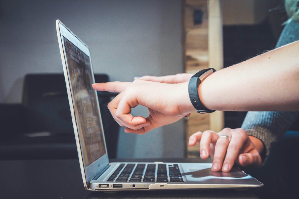 hand pointing with finger at the screen of a gray laptop