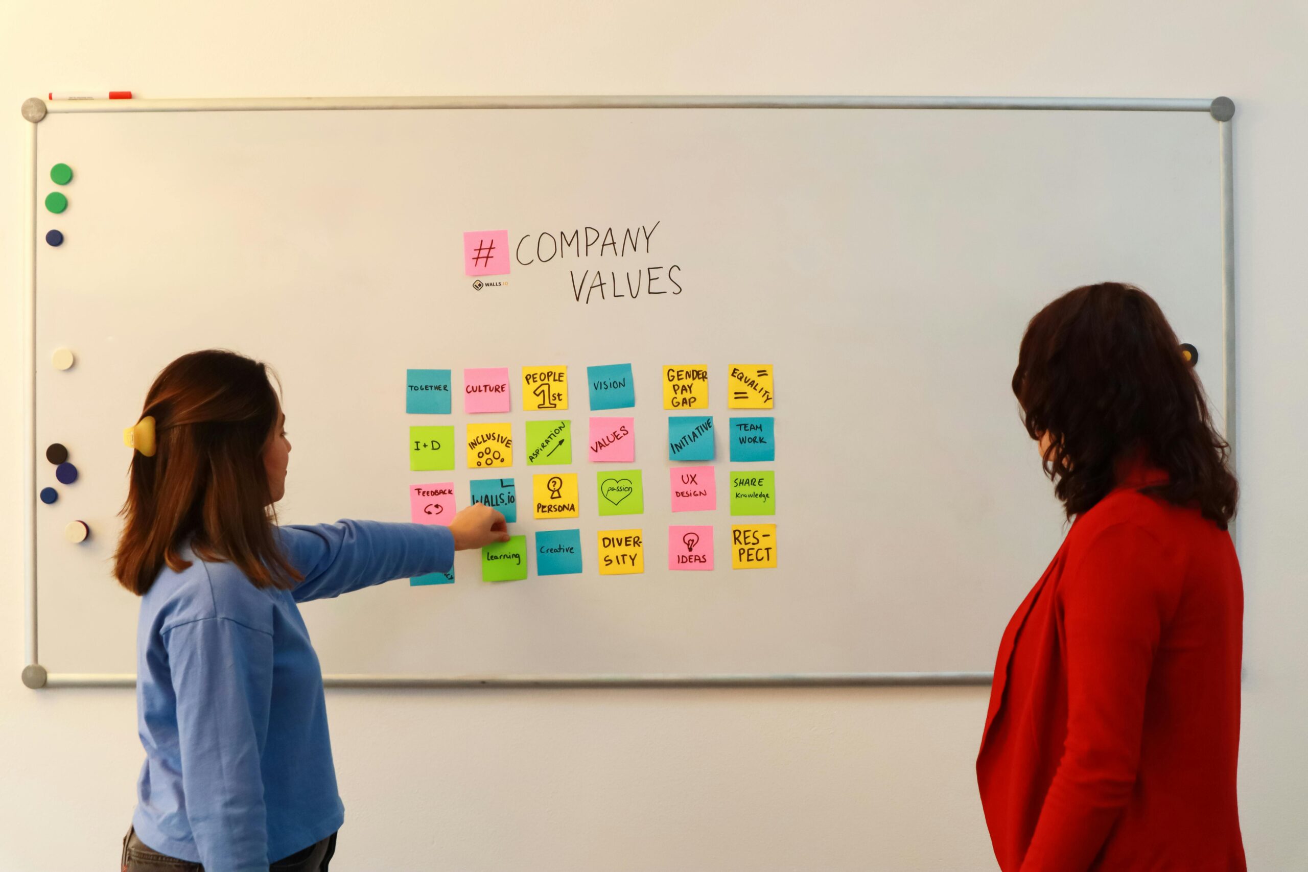 pexels-photo-15543028-15543028 Two women in an office discussing company values on a whiteboard.